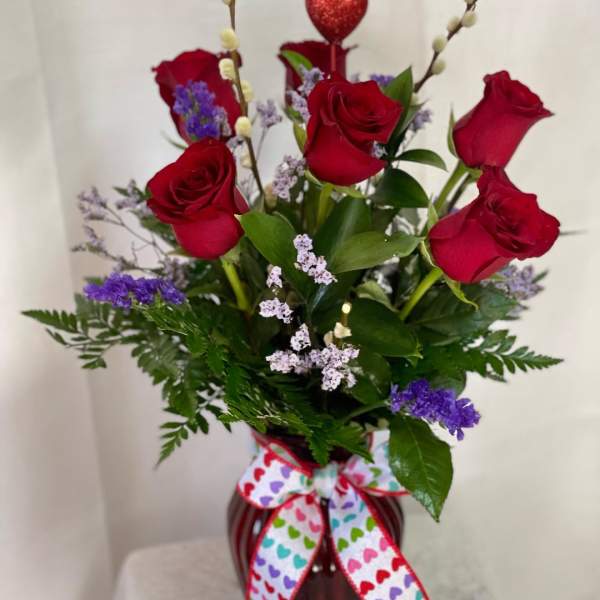 Red roses in a vase with purple filler and a heart pick