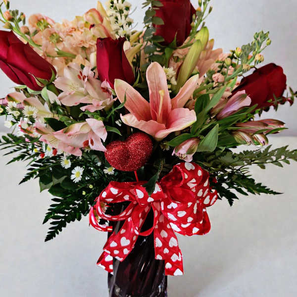 Bouquet of red roses and pink lilies in a dark vase with a heart ribbon