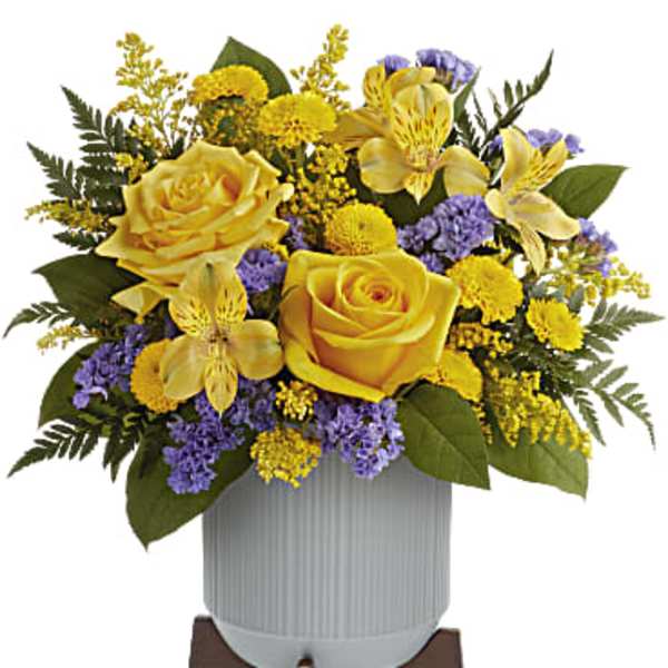 Yellow and purple flower arrangement in a white ribbed pot on a wooden stand