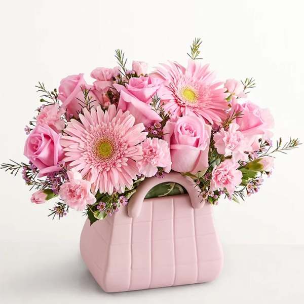 Pink roses and gerbera daisies in a pink handbag-shaped vase