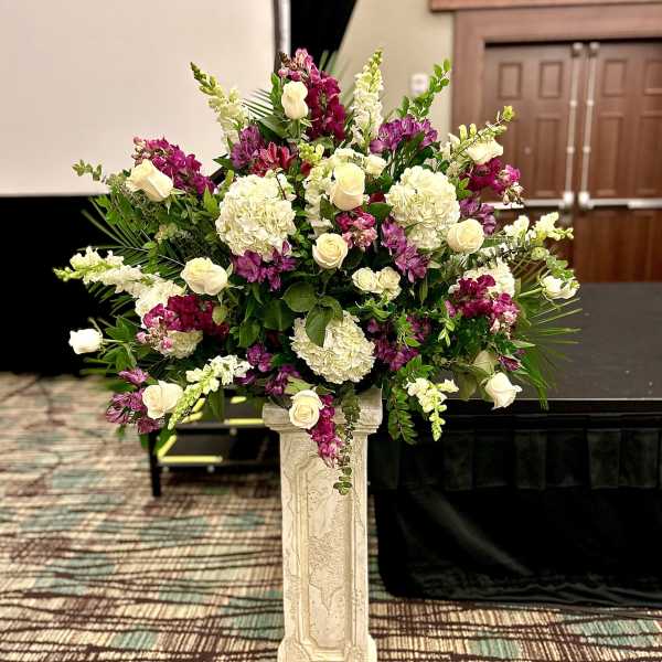 Large floral arrangement with white roses, hydrangeas, and purple blooms on a pedestal.