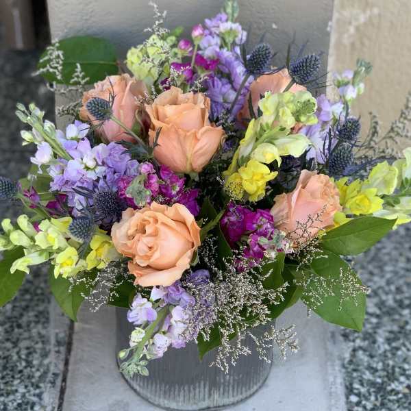 Peach roses and purple flowers in a ribbed metal vase