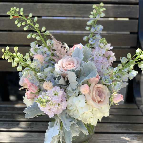 Pastel bouquet of roses, hydrangeas, and tall blue flowers in a glass vase
