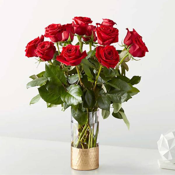Red roses arranged in a clear glass vase with a gold base