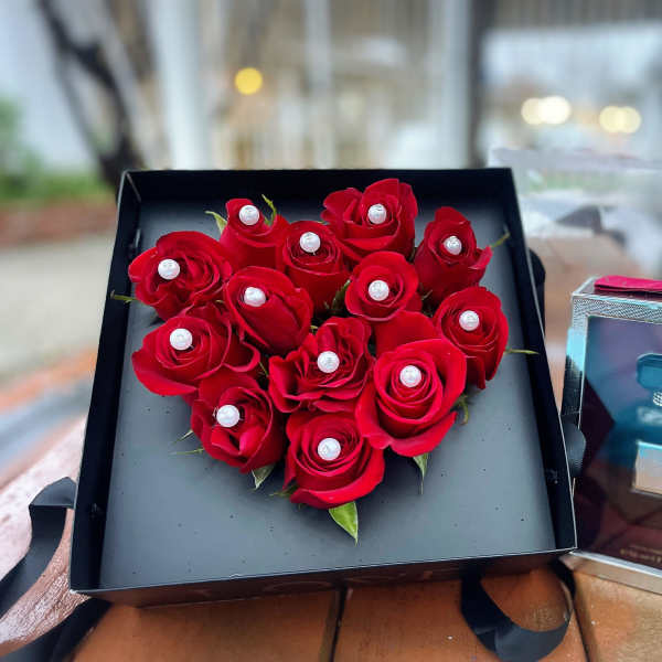 Heart-shaped box of red roses beside a perfume gift box