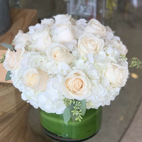 White roses and hydrangeas arranged in a green glass vase