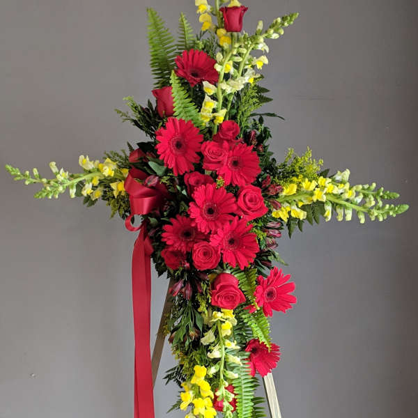 Standing floral cross with red roses, gerbera daisies, and yellow snapdragons