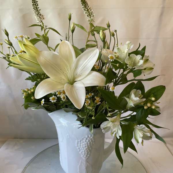 White lilies and small white flowers in a white ceramic vase