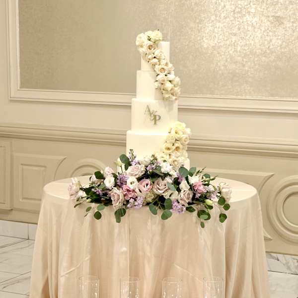 Four-tier white wedding cake with blush flowers and candles on the floor