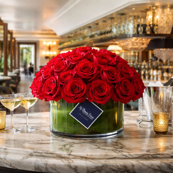 Large dome of red roses in a glass vase on a marble table with champagne glasses