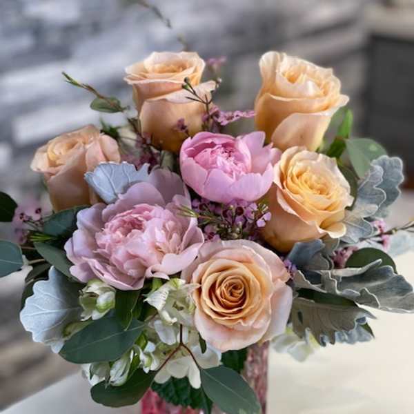 Peach and pink roses arranged in a pink glass vase