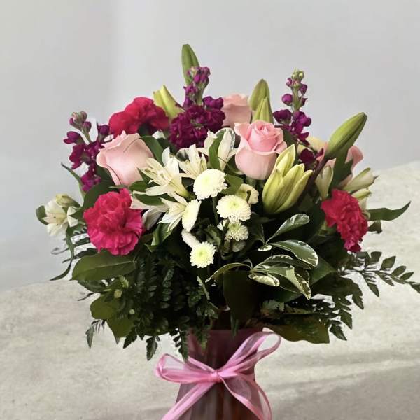Pink and white mixed flower bouquet in a pink vase with a ribbon
