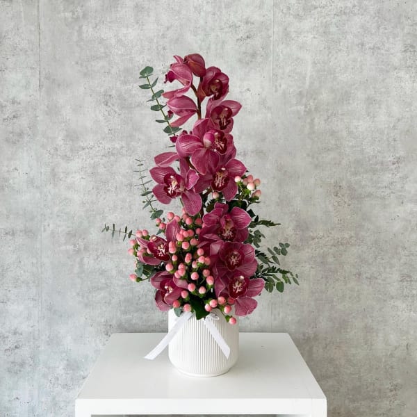 Tall pink orchid arrangement in a white ribbed vase with a ribbon