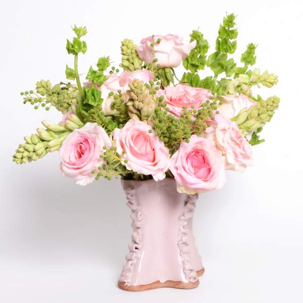 Pink roses and green filler flowers arranged in a pale pink vase