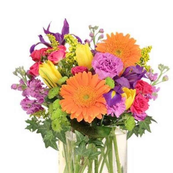 Bright mixed bouquet of orange gerbera daisies, yellow tulips and purple blooms in a clear glass cube vase