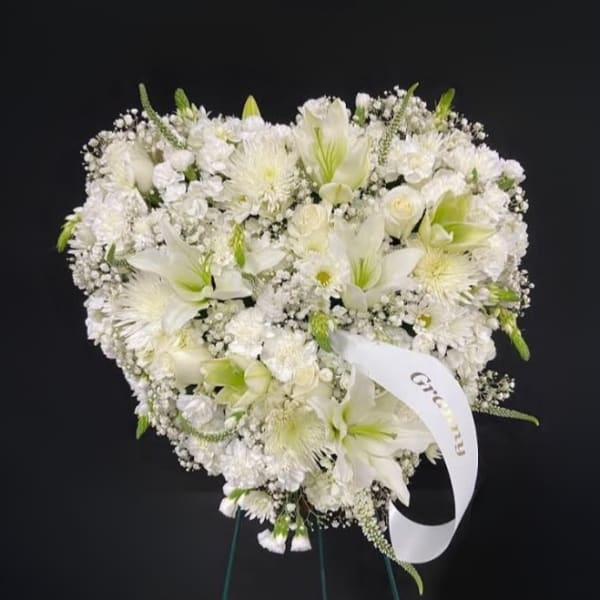 Heart-shaped standing arrangement of white flowers with a memorial ribbon on an easel.
