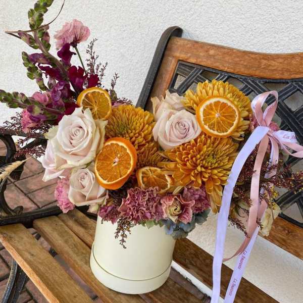 Bouquet of pale roses and yellow chrysanthemums with dried orange slices in a white box