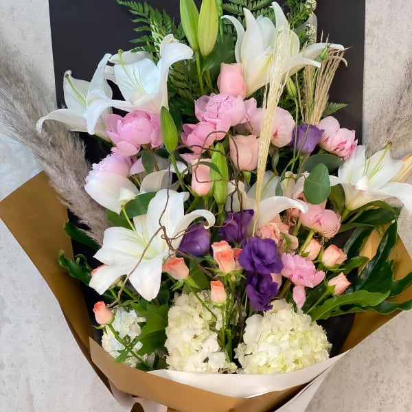 Large bouquet of white lilies, pink blooms, and purple flowers wrapped in paper