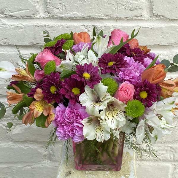 Mixed bouquet of pink, purple, white, and orange flowers in a pink glass vase