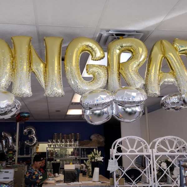 Gold balloon letters spelling CONGRATS hang overhead with silver balloons below.