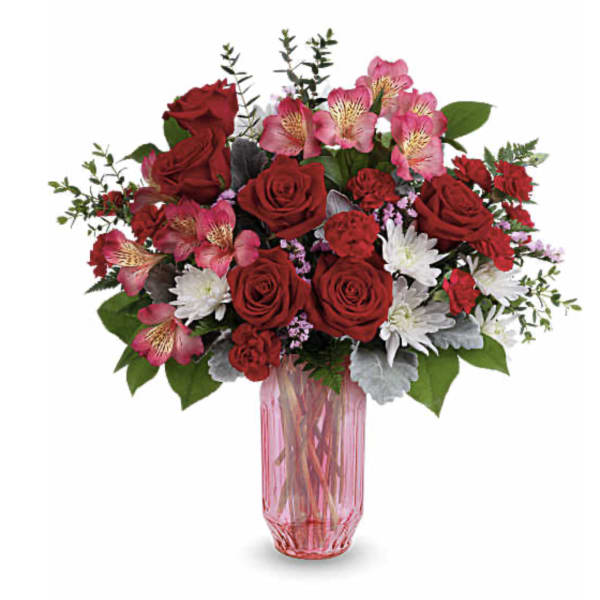 Bouquet of red roses, pink alstroemeria, and white daisies in a pink glass vase