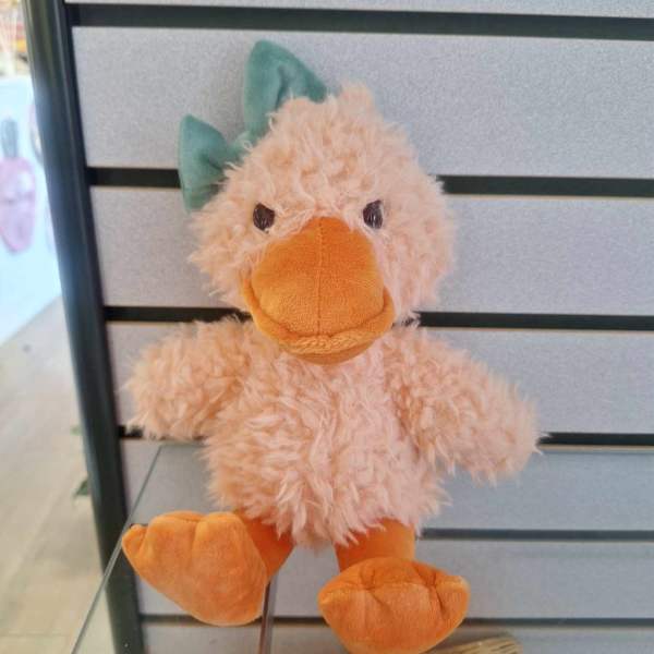 Small plush duck toy with fuzzy peach body, orange beak and feet, and a green bow.