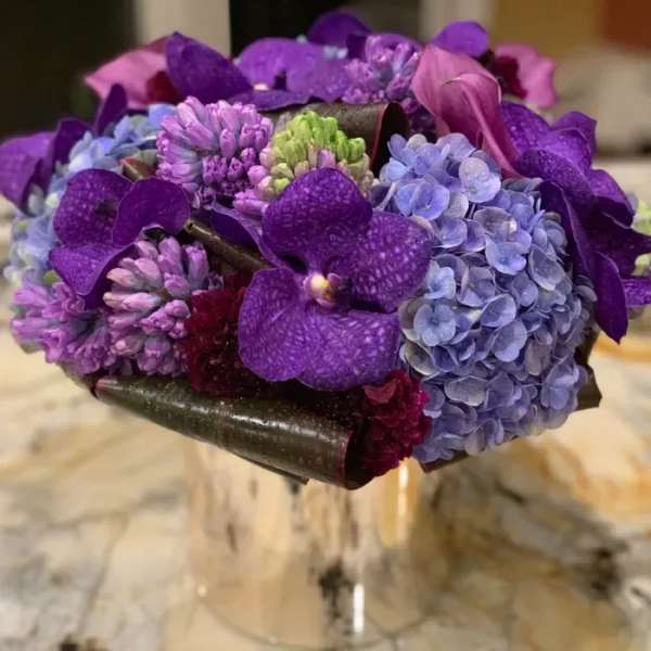 Purple bouquet with hydrangeas and orchids in a clear vase