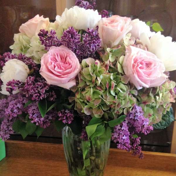 Pink roses and white blooms arranged in a clear glass vase with purple flowers