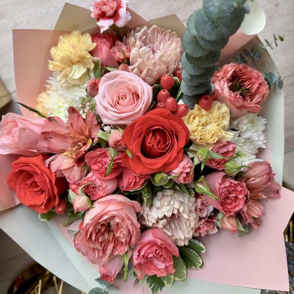 Bouquet of pink and red roses with mixed blooms wrapped in pastel paper