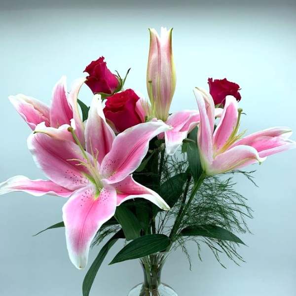 Pink lilies and red roses arranged in a clear glass vase