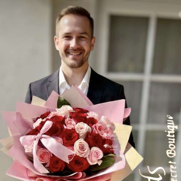 Man holding a large bouquet of red and pink roses wrapped in pink paper