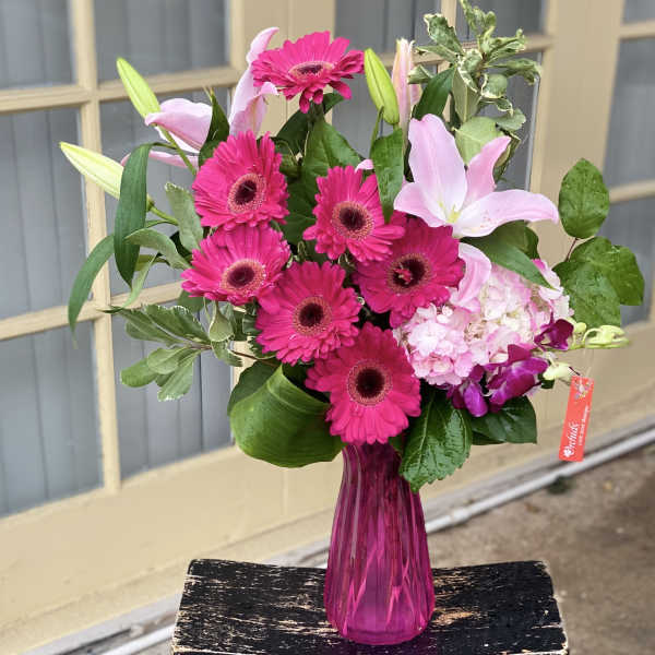 Pink gerberas and lilies in a magenta glass vase
