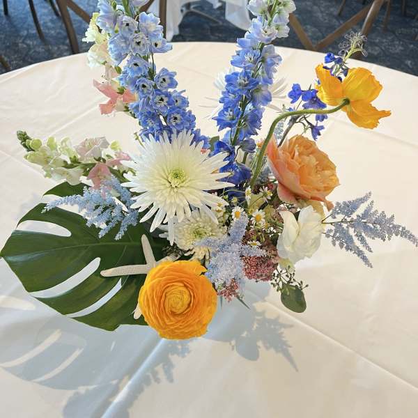 Colorful floral centerpiece with tall blue blooms and orange roses on a white table