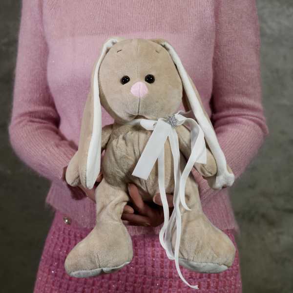 Person holding a beige plush bunny with a white ribbon