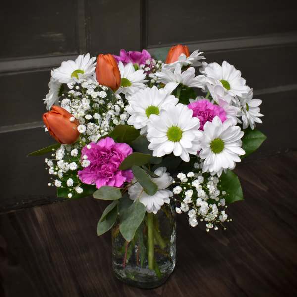 Bouquet of white daisies, orange tulips, and pink carnations in a glass vase