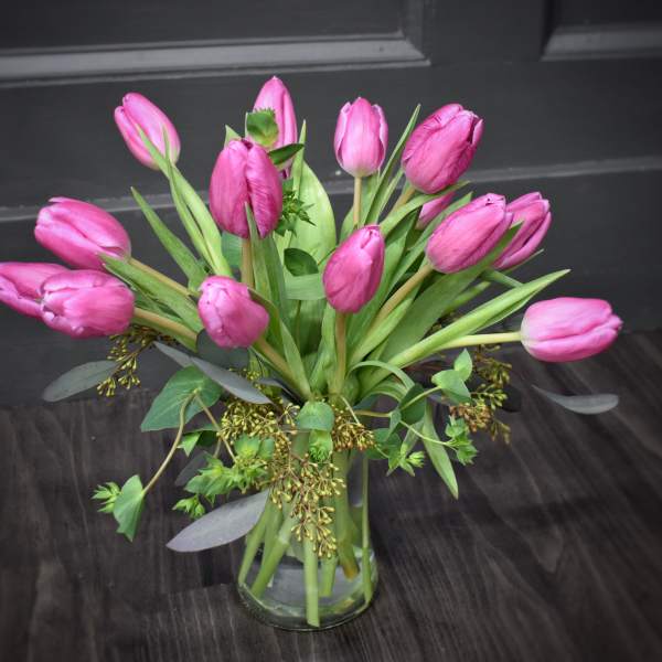 Pink tulips arranged in a clear glass vase with mixed greenery