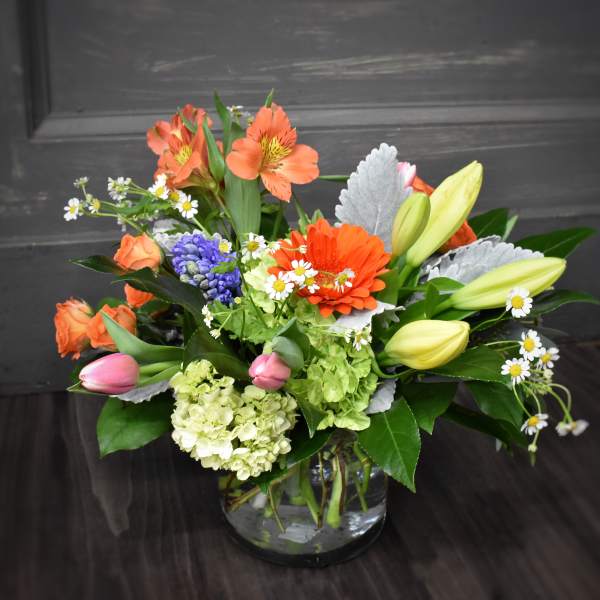 Mixed bouquet with orange blooms, lilies, and daisies in a glass vase