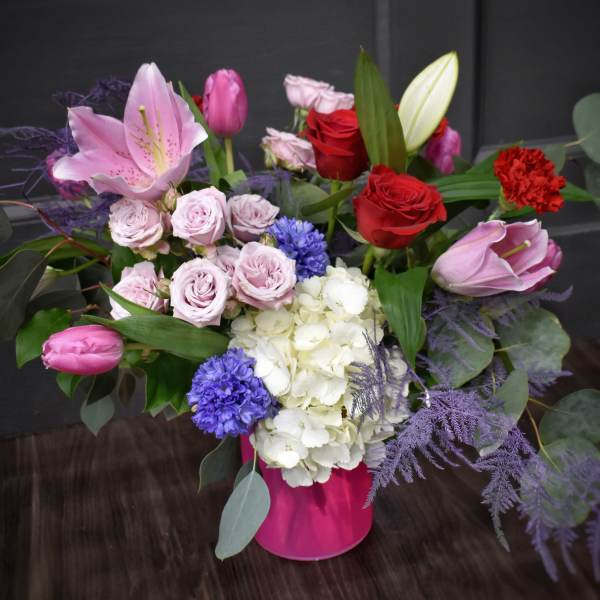 Mixed bouquet with pink lilies, red roses, and white hydrangeas in a pink vase
