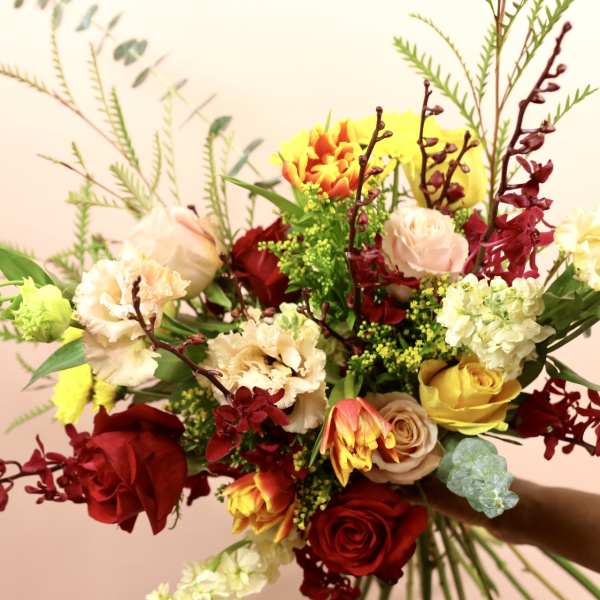 Handheld bouquet of red, yellow, and blush flowers with long burgundy stems