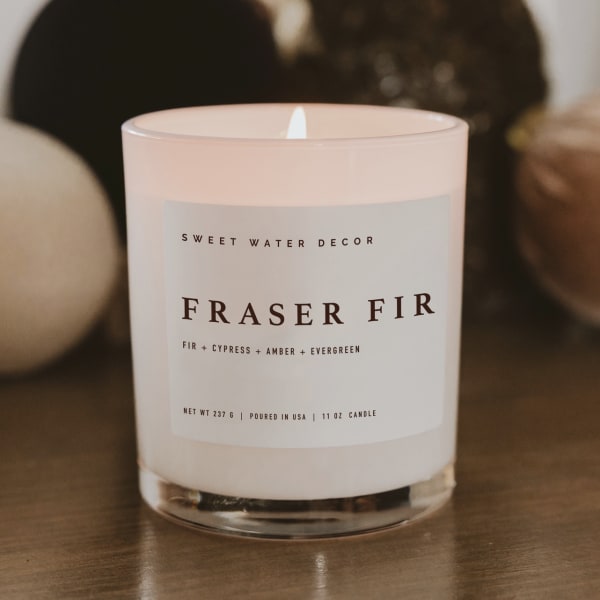 Pink glass candle labeled Fraser Fir with a lit wick