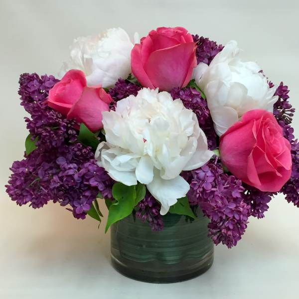 Pink roses and white peonies in a glass vase with purple lilacs