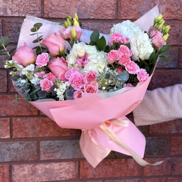 Pink and white bouquet of roses, carnations, and hydrangeas wrapped in pink paper