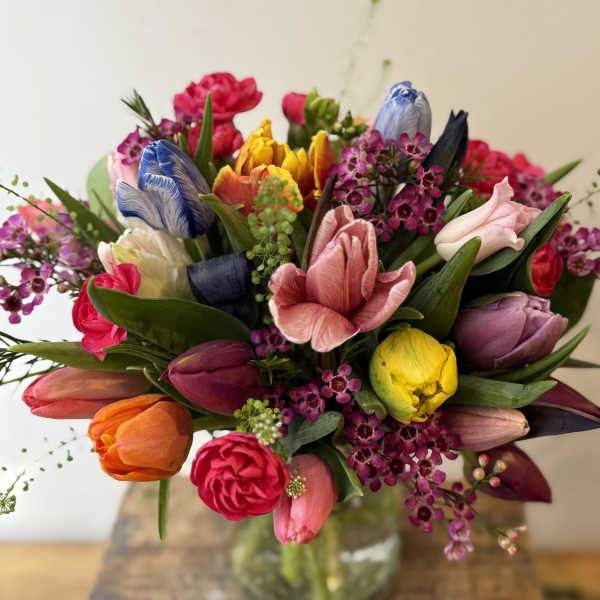 Colorful bouquet of tulips and small purple flowers in a glass vase