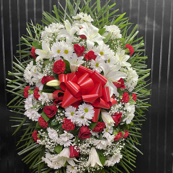 Oval floral wreath with white lilies, daisies, and red roses, finished with a red bow