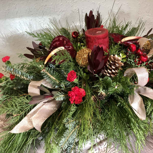Holiday centerpiece with red candle, pinecones, ribbons, and evergreen branches