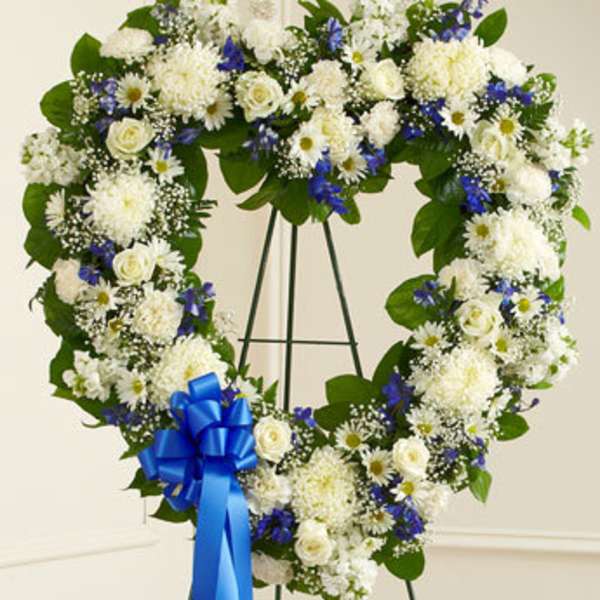 Heart-shaped floral wreath with white and blue flowers on a stand