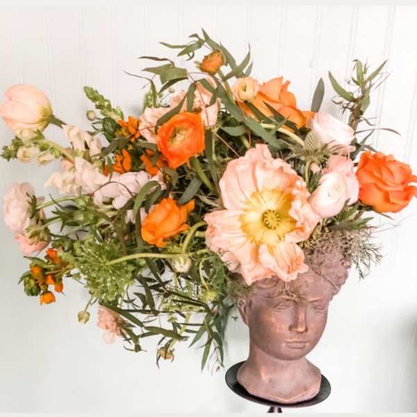 Orange and blush flowers arranged in a sculpted head vase