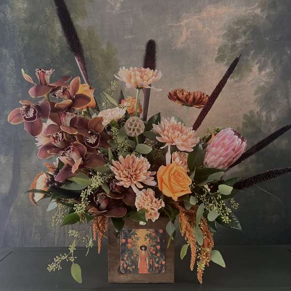 Large floral arrangement with orchids, chrysanthemums, and a peach rose in a wooden container