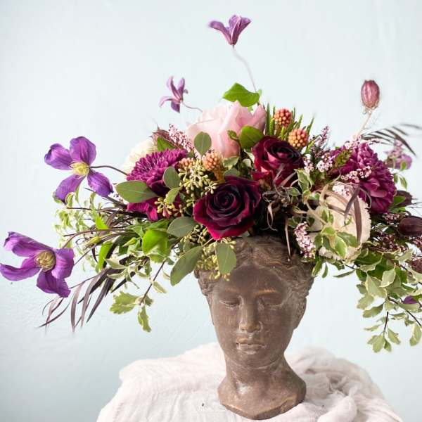 Floral arrangement in a sculpted head vase with purple and pink blooms