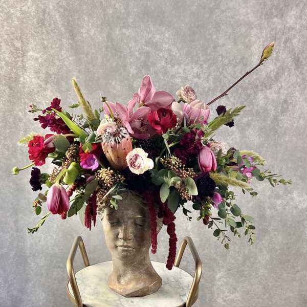 Large floral arrangement in a sculpted bust vase with pink and burgundy blooms